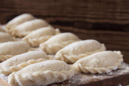 Prepared for cooking vareniki, dumplings, pierogi on a floured wooden board - traditional Ukrainian food. Selective focusの写真素材