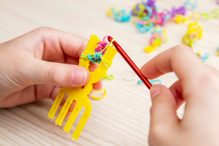 Rubber Band Weaving. Knitting rubber bands with loom knit. Hands of girl weaving wristband of rubber...