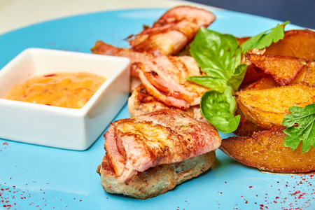 Pork in bacon with baked potatoes on a blue plate. Close-up, selective focus