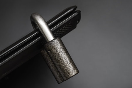Locked steel padlock in a drilled hole of the black laptop on dark background. Concept of protecting personal data on a computer. A laptop is locked with a lock. Closeup, selective focusの写真素材