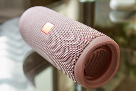 A part of portable pink wireless speaker on a glass surface. Close-up, selective focus