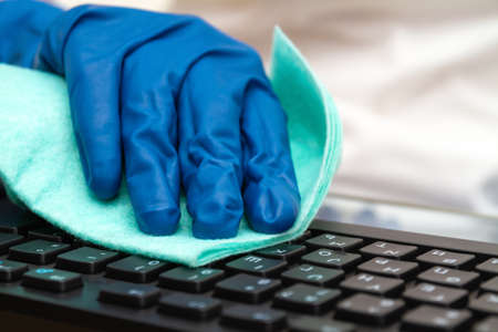 Girl's hand in blue protective glove cleans keyboard with a cloth for prevention coronavirus, bacteria, viruses and germs.の写真素材
