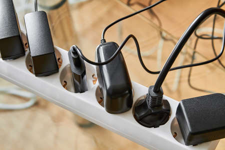Electrical power strip overloaded with multiple electrical cords plugged in. Many plugs plugged into electric power barの写真素材