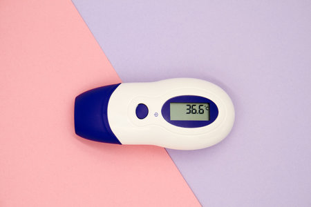 A non-contact infrared thermometer on a colorful background showing temperature 36.6