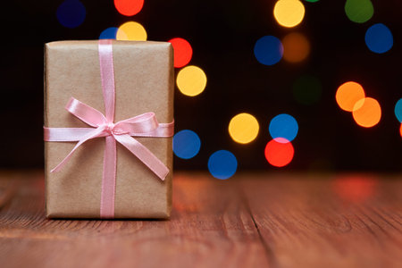 Christmas or New Year gift box on a wooden surface against a background of colorful lights