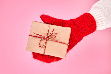 A child in a mitten holds a Christmas or New Year gift box against a pink background