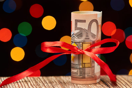 A roll of 50 euro bills on wooden surface against a background of colorful Christmas lights. Money...
