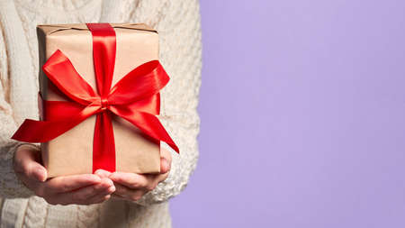 Girl holding a Christmas or New Year gift box with a red ribbon on a purple backgroundの写真素材