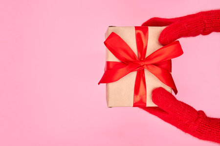 A child in a mittens holds a Christmas or New Year gift box against a pink backgroundの写真素材
