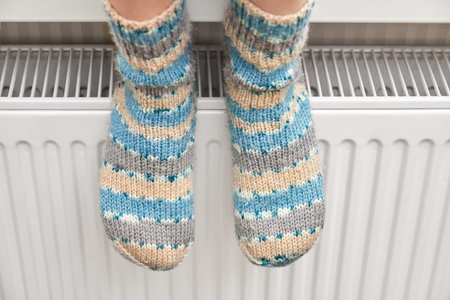 A girl in blue woolen socks warms her feet on the radiator