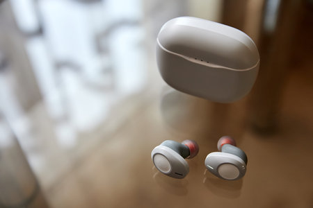 White wireless headphones and closed charge box on a glass surfaceの写真素材