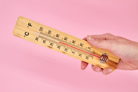 A girl holding a household alcohol thermometer in her hand on pink background showing temperature in...