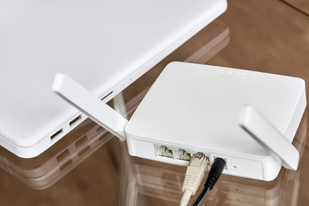 White wireless router near a laptop on a glass table.