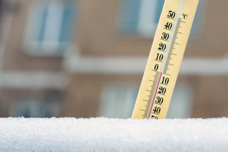 Wintertime. Thermometer in the snow shows temperature is about zero against the background of a multi-storey building. Concept of weather forecast.の写真素材