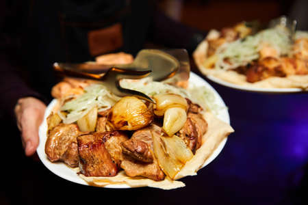 Waiter holds plates of fried pork barbecue, pita and onion. Close-up, selective focusの写真素材
