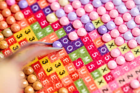 Girl collect diamond painting. Diamond embroidery with a tweezers. Acrylic rhinestones. Close-up, selective focusの写真素材