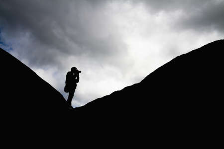 Silhouette of a man in the mountains is taking pictures of the landscapeの写真素材