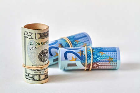 Twenty dollar bill rolled up as a tubule stands on the background of twenty euro bills. Concept of dollar superiority over euro. Closeup, selective focusの写真素材