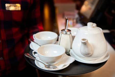 The waiter holds in his hand a tray with a kettle, tea cups and sugar. Close-up, selective focusの写真素材