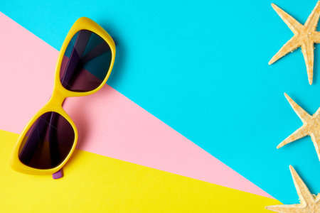 Sunglasses on minimal colorful background decorated with starfish with copy space