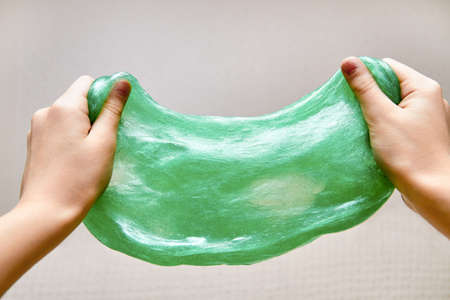 Hands stretch green slime on light background. Toy antistress. Toy for the development of hand motor skills. Closeup, selective focusの写真素材