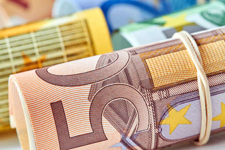 Fifty Euro bill rolled up as a tubule lies on the background of euro bills. Fifty Euro banknote details in a macro shot. Closeup, selective focusの写真素材