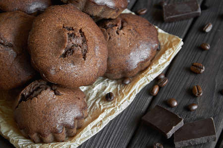A group of homemade chocolate muffins on parchment with coffee beans and pieces of chocolate. Dark wooden background, closeup, selective focusの写真素材