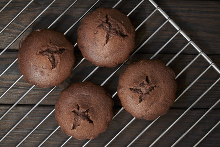 Homemade chocolate muffins on metal oven grill. Dark wooden background, top view