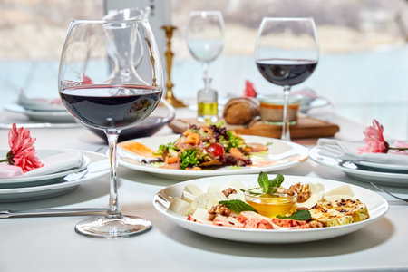 A served restaurant table with glasses of red wine and appetizer awaits guests. Close-up, selective...