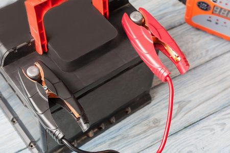 A car battery with red and black battery jumper clamps and car battery charger on the background....