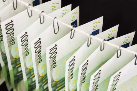 Parts of hundred euro bills are hanging on clerical clips on a rope on the dark background. Closeup, selective focusの写真素材