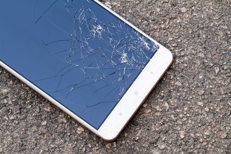 Smartphone with broken blue display screen is lying on the asphalt. Closeup, selective focus