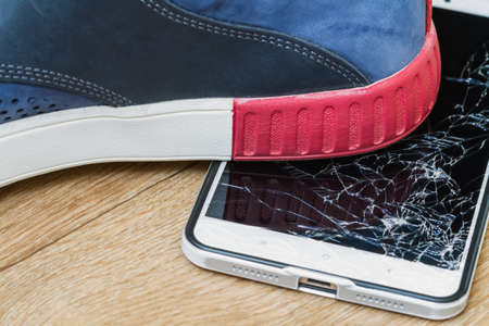Smartphone display smashed by boot on brown background. Closeup, selective focusの写真素材