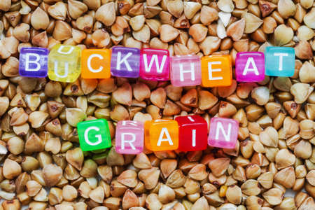 Background from buckwheat grain with the inscription of buckwheat grain in colored letters on cubes. Closeup, top viewの写真素材