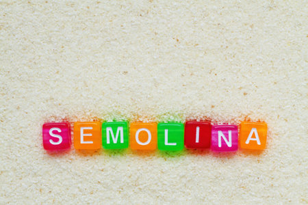 Background from semolina with the inscription of semolina in colored letters on cubes. Closeup, top...