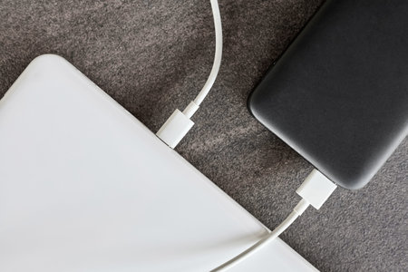 Power bank charges a laptop via USB type C cable on gray stone background