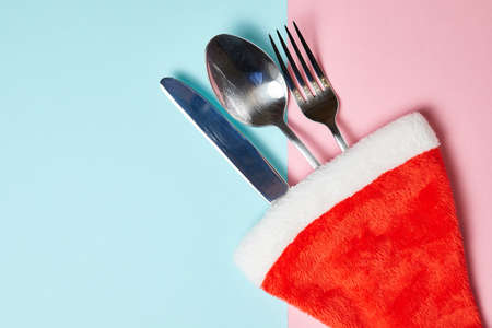 Knife, fork and spoon in santa hat on pink and blue background with copy spaceの写真素材
