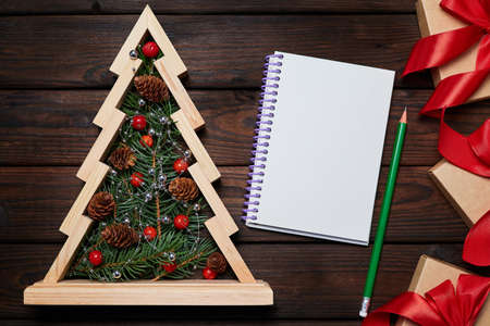 Wooden christmas tree with Fir branches inside, gift boxes with red ribbons and a Blank notepad on wooden backgroundの写真素材