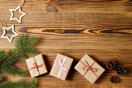 Christmas gift boxes with fir branches, pine cones and wooden stars on wooden background