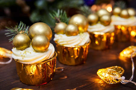 Christmas cupcakes decorated with chocolate christmas balls and and a spruce branch on a background of glowing garlandsの写真素材