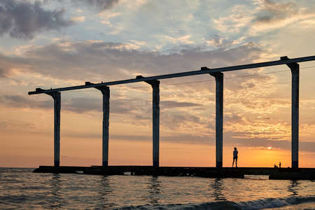 Sea pier at sunset, where a girl is sunbathing and fishermen are fishingの写真素材