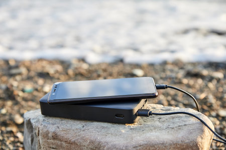 Powerbank charges the phone on the beach by the sea