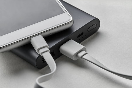 The smartphone is charging from external power bank with cable. White background, closeup, selective...