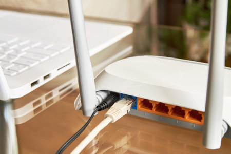 White wireless wi-fi router near a laptop on a glass table