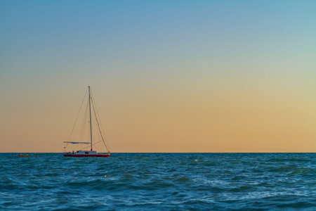 A small sailboat floats in the sea at sunset