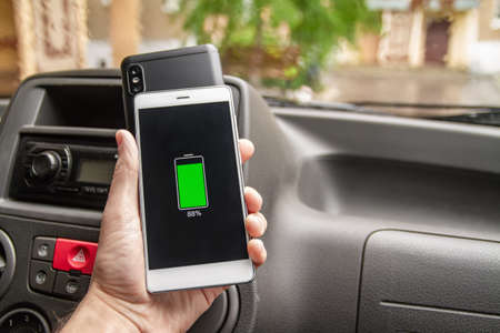 Phone battery wireless charge sharing technology. Wireless charge sharing smartphone in the car in rainy weatherの写真素材