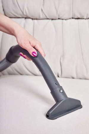 Close-up of a female hand vacuums the surface of the beige sofaの写真素材