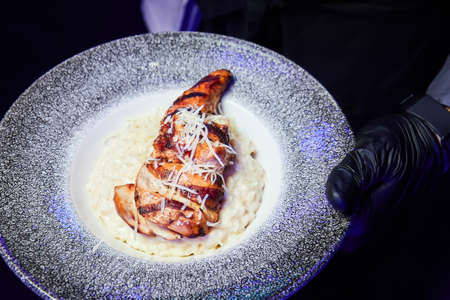 Waiter holding a plate of chicken steak with cheese risottoの写真素材
