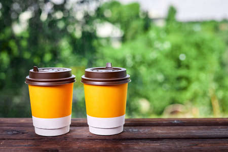 Takeaway cups for drink on a wooden surface against the background of green foliageの写真素材