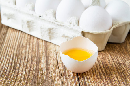 Close-up of fresh egg yolk on the background of eggs in paper tray on wooden surface